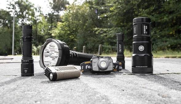 A range of tactical flashlights, a headlamp and a lantern on a paved path